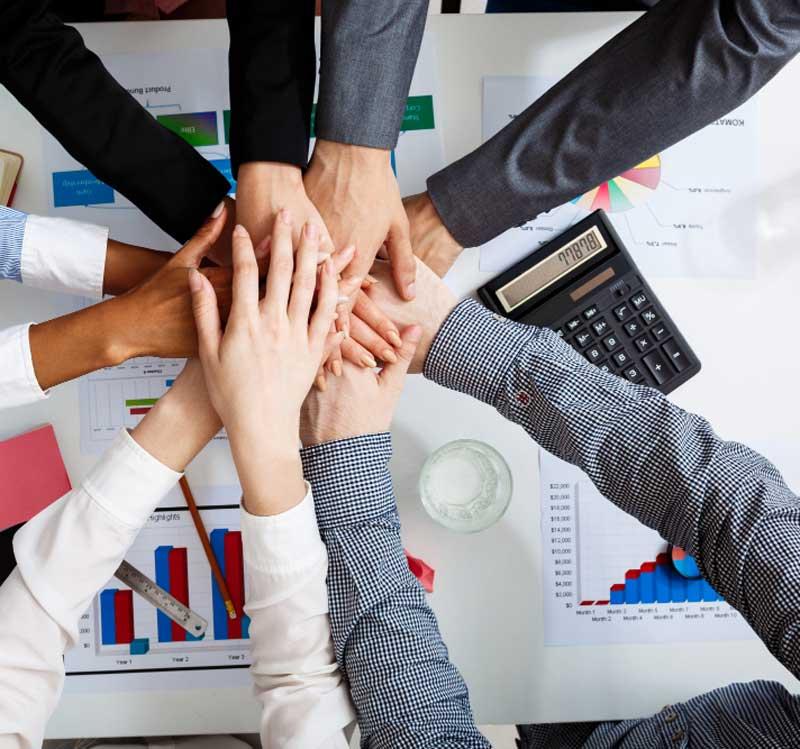 Colleagues joining hands above a shared work table